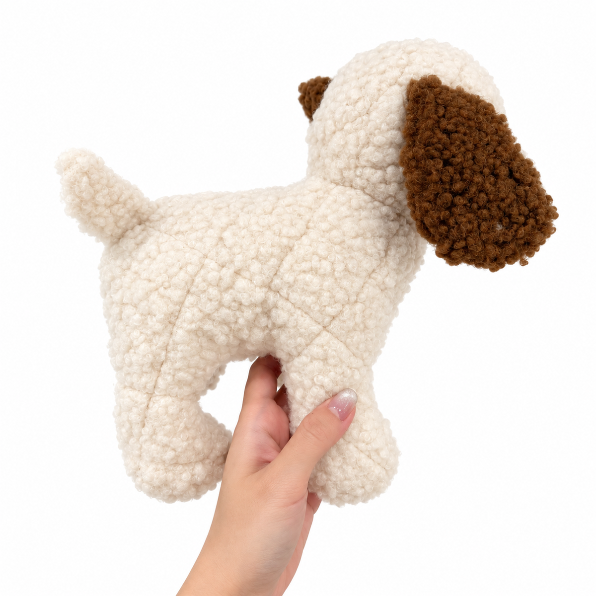 Cream curly plush dog toy held in hand for scale